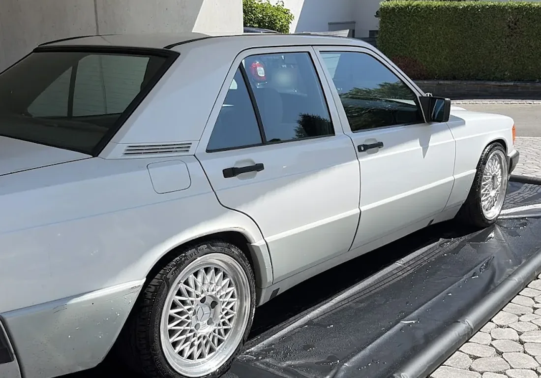 Weisser Mercedes 190 E mit sauberen Felgen nach der Handwäsche, auf der Waschmatte vor dem Haus